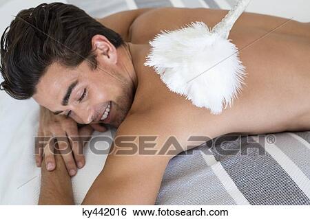 Man lying on bed with feather duster on back View Large Photo Image Stock Photograph - Man lying on bed with feather duster on back. Fotosearch
