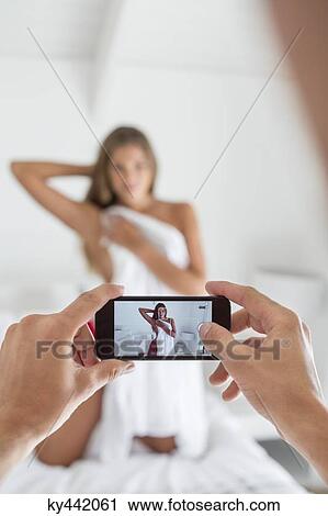 Stock Image - Man taking picture of his girlfriend in the bedroom. Fotosearch