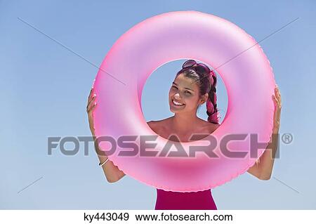 Stock Photo - Beautiful woman looking through an inflatable ring on the beach. Fotosearch