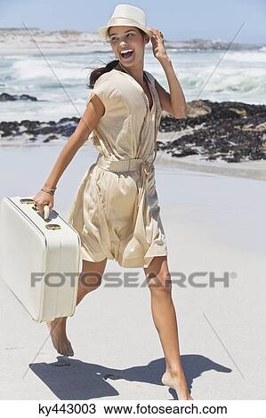 Stock Image - Beautiful woman running with a suitcase on the beach. Fotosearch