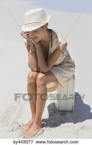 Stock Photo - Beautiful woman sitting on a suitcase on the beach. Fotosearch