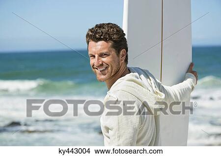 Man holding a surfboard on the beach View Large Photo Image Picture - Man holding a surfboard on the beach. Fotosearch