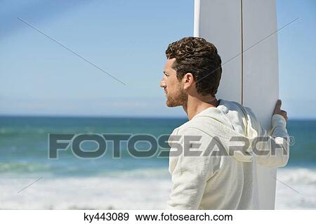 Stock Photo - Man holding a surfboard on the beach. Fotosearch