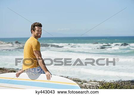 Man sitting on a surfboard on the beach View Large Photo Image Stock Image - Man sitting on a surfboard on the beach. Fotosearch