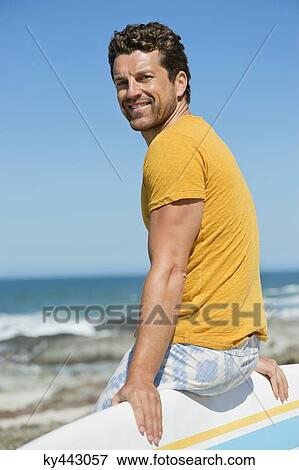Stock Photo - Man sitting on a surfboard on the beach. Fotosearch