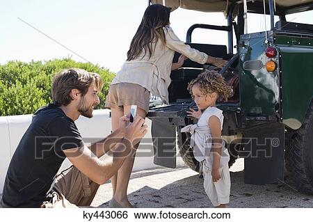 Man taking a picture of his daughter with a smartphone beside a SUV View Large Photo Image Stock Photograph - Man taking a picture of his daughter with a smartphone beside a SUV. Fotosearch