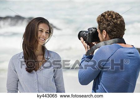 Man taking a picture of his wife with a camera on the beach View Large Photo Image Stock Photography - Man taking a picture of his wife with a camera on the beach. Fotosearch