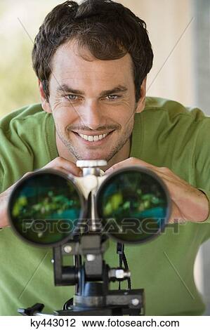 Stock Image - Smiling man looking through binoculars. Fotosearch