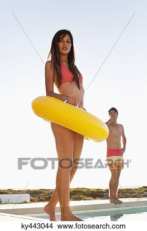 Woman walking with inflatable ring at the poolside with a man behind her View Large Photo Image Picture - Woman walking with inflatable ring at the poolside with a man behind her. Fotosearch
