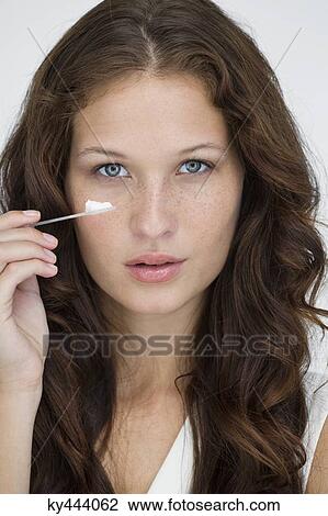 Stock Image - Portrait of a woman applying moisturizer cream on her face. Fotosearch