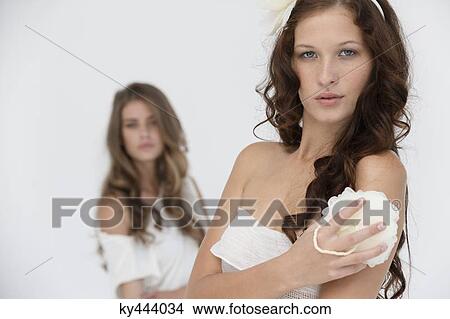 Woman holding a flower sponge with her friend in the background View Large Photo Image Picture - Woman holding a flower sponge with her friend in the background. Fotosearch