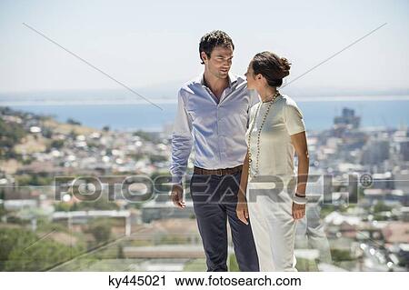 Stock Image - Couple looking at each other on a terrace with city in the background. Fotosearch