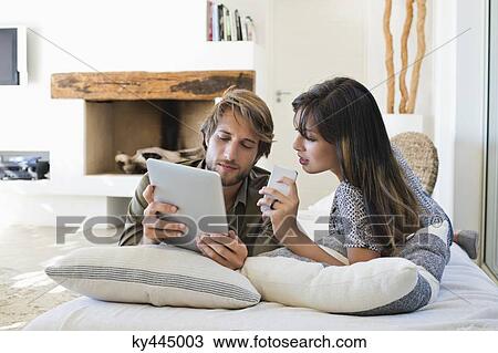 Couple lying on the bed and using electronic gadgets View Large Photo Image Stock Image - Couple lying on the bed and using electronic gadgets. Fotosearch