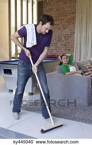 Man cleaning floor with a mop and his wife watching television in the background View Large Photo Image Stock Image - Man cleaning floor with a mop and his wife watching television in the background. Fotosearch