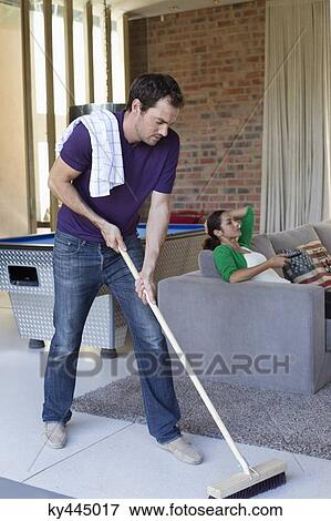 Man cleaning floor with a mop and his wife watching television in the background View Large Photo Image Stock Photo - Man cleaning floor with a mop and his wife watching television in the background. Fotosearch