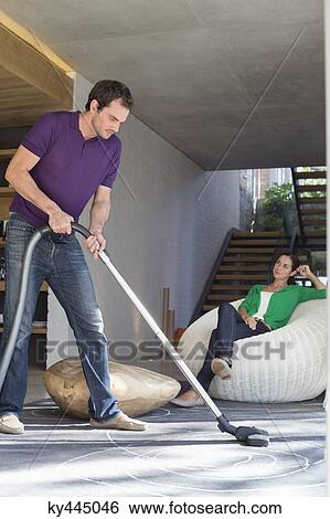 Man cleaning house with a vacuum cleaner with his wife sitting on a seat View Large Photo Image Stock Photograph - Man cleaning house with a vacuum cleaner with his wife sitting on a seat. Fotosearch