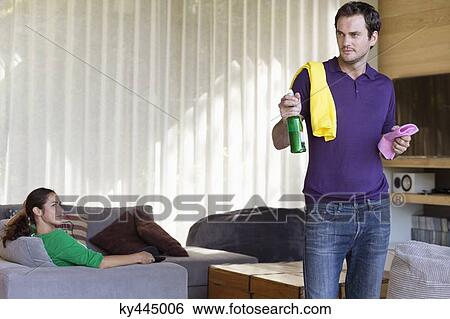 Man holding cleaning equipment with his wife sitting on a couch View Large Photo Image Stock Photograph - Man holding cleaning equipment with his wife sitting on a couch. Fotosearch