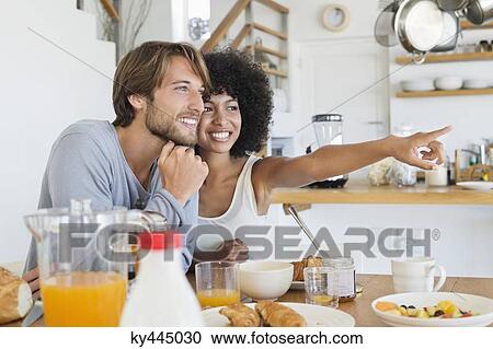 Stock Image - Smiling couple sitting at a dining table. Fotosearch