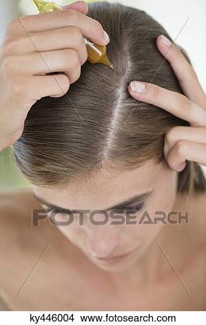 Picture - Woman applying oil into her hair. Fotosearch