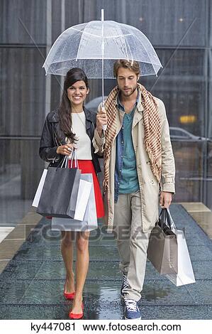 Couple with shopping bags sheltering under umbrella in rain View Large Photo Image Stock Image - Couple with shopping bags sheltering under umbrella in rain. Fotosearch