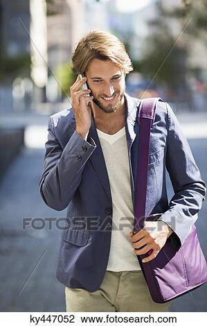 Stock Image - Man walking on a street and talking on a mobile phone. Fotosearch
