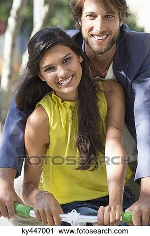 Stock Image - Portrait of a smiling couple riding a bicycle. Fotosearch