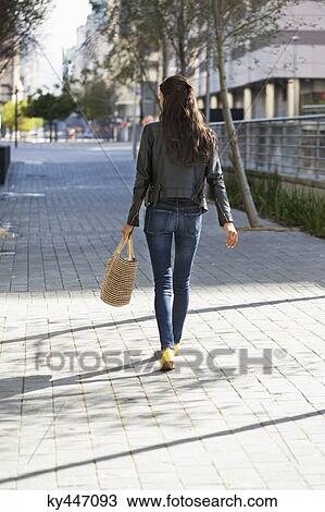 Stock Image - Rear view of a woman walking with a handbag. Fotosearch