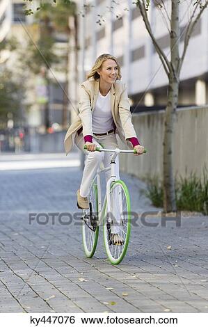 Woman riding a bicycle on a street and smiling View Large Photo Image Stock Photograph - Woman riding a bicycle on a street and smiling. Fotosearch