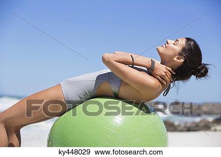 Stock Photo - Beautiful woman exercising with fitness ball on the beach. Fotosearch