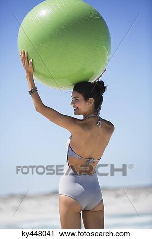 Stock Image - Beautiful woman holding a fitness ball on the beach. Fotosearch