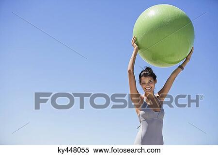 Stock Photography - Beautiful woman holding a fitness ball on the beach. Fotosearch