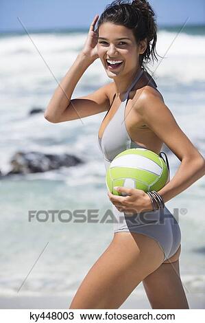 Stock Image - Beautiful woman holding a volleyball on the beach. Fotosearch