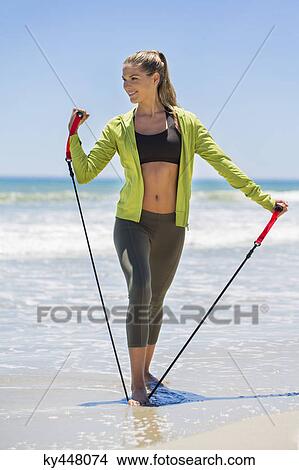 Smiling woman exercising with a chest expander on the beach View Large Photo Image Picture - Smiling woman exercising with a chest expander on the beach. Fotosearch