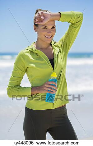 Smiling woman holding a water bottle on the beach View Large Photo Image Stock Photograph - Smiling woman holding a water bottle on the beach. Fotosearch