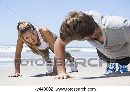 Stock Image - Woman exercising on the beach with her coach. Fotosearch