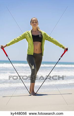 Stock Photograph - Woman exercising with a chest expander on the beach. Fotosearch