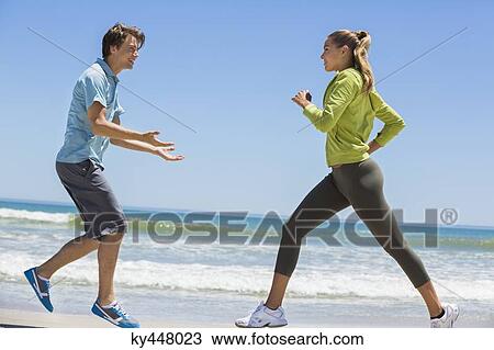 Stock Image - Woman jogging on the beach with her coach. Fotosearch
