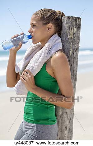 Woman leaning against a wooden post on the beach drinking water View Large Photo Image Stock Photo - Woman leaning against a wooden post on the beach drinking water. Fotosearch