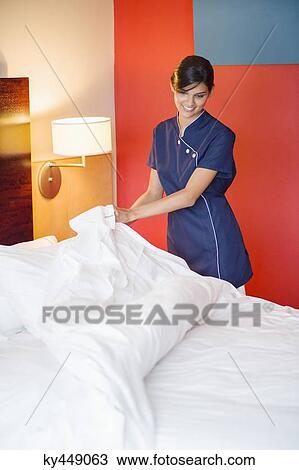 Stock Image - Maid making a bed in a hotel room. Fotosearch