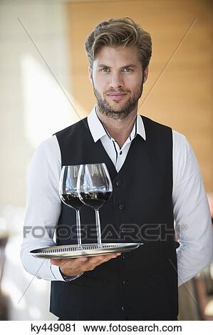 Stock Image - Portrait of a waiter holding a tray of wine glasses in a restaurant. Fotosearch