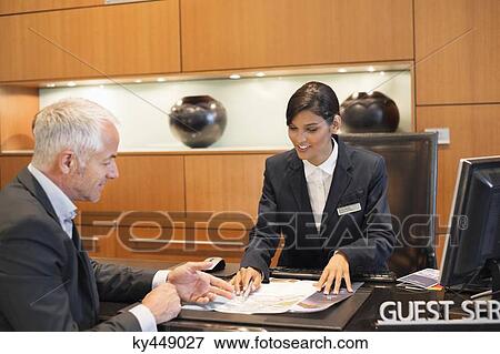 Stock Photo - Receptionist showing a brochure to a businessman at a hotel reception counter. Fotosearch