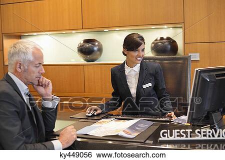 Receptionist working on a desktop pc with a businessman at the hotel reception counter View Large Photo Image Stock Photograph - Receptionist working on a desktop pc with a businessman at the hotel reception counter. Fotosearch