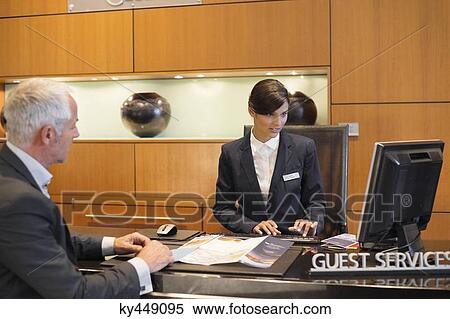 Receptionist working on a desktop pc with a businessman at the hotel reception counter View Large Photo Image Stock Photography - Receptionist working on a desktop pc with a businessman at the hotel reception counter. Fotosearch