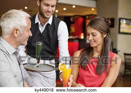 Waiter serving drinks to a couple in a restaurant View Large Photo Image Stock Photo - Waiter serving drinks to a couple in a restaurant. Fotosearch