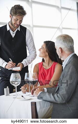 Stock Image - Waiter taking orders from a couple in a restaurant. Fotosearch