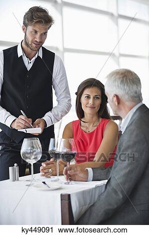 Waiter taking orders from a couple in a restaurant View Large Photo Image Stock Image - Waiter taking orders from a couple in a restaurant. Fotosearch