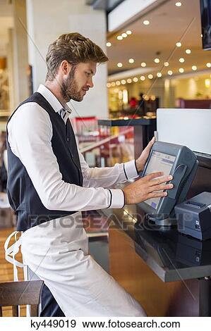 Stock Photo - Waiter using a computer at checkout counter in a restaurant. Fotosearch