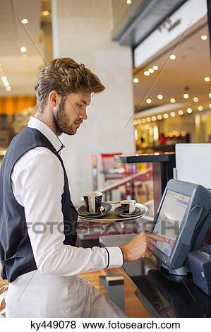Waiter using a computer at checkout counter in a restaurant View Large Photo Image Stock Photo - Waiter using a computer at checkout counter in a restaurant. Fotosearch