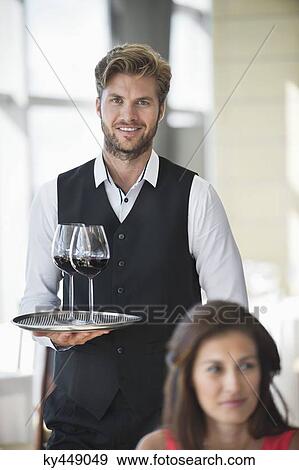 Stock Photo - Woman sitting in a restaurant with a waiter holding a tray of wine glasses in the background. Fotosearch