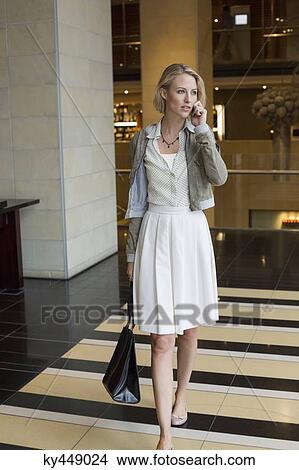 Woman talking on a mobile phone while walking on an airport View Large Photo Image Picture - Woman talking on a mobile phone while walking on an airport. Fotosearch
